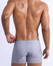 Back view of a male model wearing men’s beach trunks in stone grey color by the Bang! Clothes brand of men's beachwear from Miami.