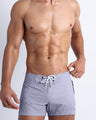 Male model wearing the GRAY ANATOMY men’s swim flex shorts in pale grey color by the Bang! brand of men's beachwear from Miami.