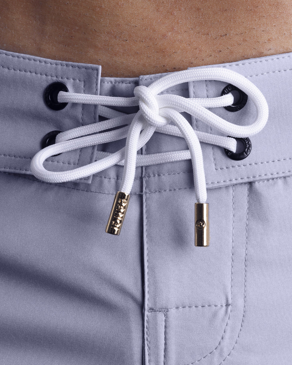 Close-up view of men’s summer beach shorts by BANG! clothing brand, showing white cord with custom branded golden cord ends, and matching custom eyelet trims in gold.
