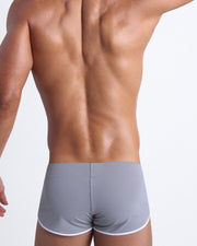 Back view of a male model wearing men’s swim shorts in stone grey color by the Bang! Clothes brand of men's beachwear.