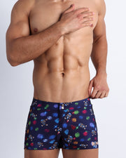 Frontal view of model wearing the HEY MISTER TJ (CLUB MIX) Men’s swimwear in dark tones with colorful headphones and disc shapes and a dj tiger print.