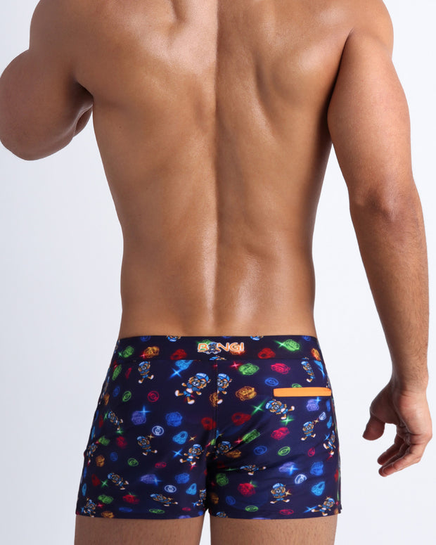 Back view of model wearing the HEY MISTER TJ (CLUB MIX) Men’s beach shorts by BANG! with clubbing and disc-jockey details in dark colors made by the Bang! official brand of men&