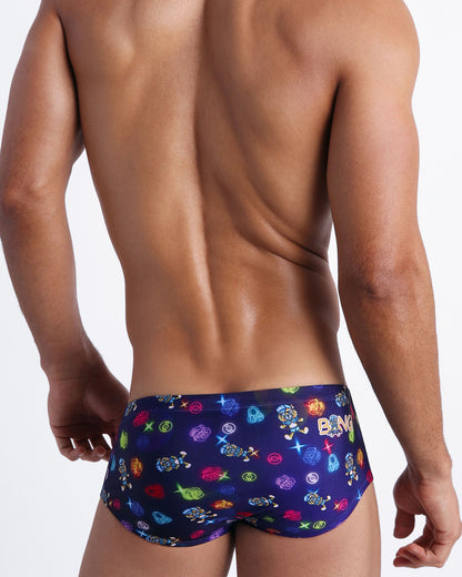 Back view of model wearing the HEY MISTER TJ (CLUB MIX) Men’s swim sunga by BANG! with clubbing and disc-jockey details in dark colors made by the Bang! official brand of men's beachwear.