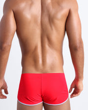 Back view of a male model wearing men’s swim shorts in neon red by the Bang! Clothes brand of men's beachwear.