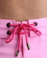 Close-up view of men’s summer beach shorts by BANG! clothing brand, showing pink cord with custom branded golden cord ends, and matching custom eyelet trims in gold.