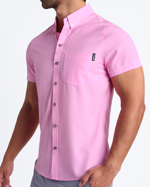 Side view of a masculine model wearing men’s Summer button down shirt in a baby pink color with official logo of BANG! Brand.