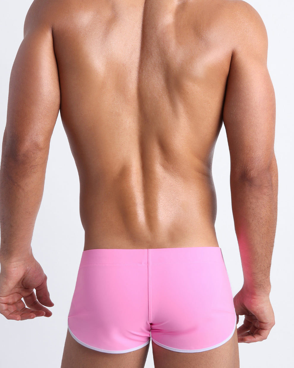 Back view of a male model wearing men’s swim mini shorts in bubble gum pink by the Bang! Clothes brand of men's beachwear.