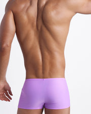 Back view of a male model wearing men’s swim trunks in neon light purple color made with Italian-made Vita By Carvico Econyl Nylon by the Bang! Clothes brand of men's beachwear.