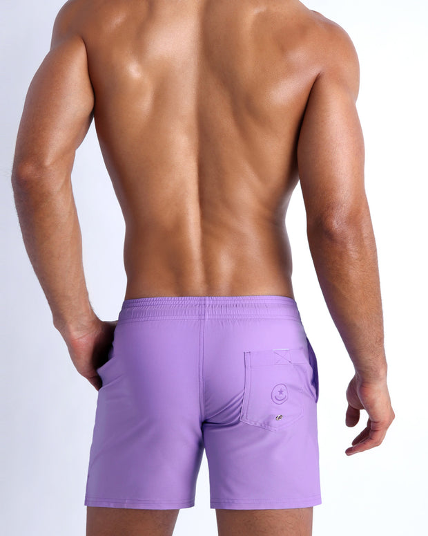 Back view of male model wearing the NEO VIOLET beach trunks for men by BANG! Miami in lilac color.