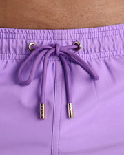 Close-up view of inseam and details of these shorts for men, with purple cord and custom branded golden cord-ends, and matching custom eyelet trims in gold.