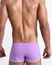 Back view of a male model wearing men’s swim shorts in neon light purple color made with Italian-made Vita By Carvico Econyl Nylon by the Bang! Clothes brand of men's beachwear.