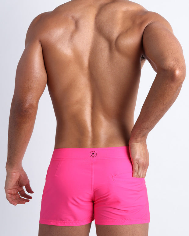 Back view of a male model wearing men’s beach trunks in hot pink color by the Bang! Clothes brand of men&