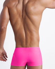 Back view of a male model wearing men’s swim trunks in hot pink color by the Bang! Clothes brand of men's beachwear from Miami.