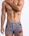 Frontal view of model wearing the SO RED THE ROSE men’s swimsuit bottoms featuring leopard print in white and black tones with red roses by the Bang! menswear brand.