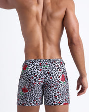 Male model's back view showing the SO RED THE ROSE beach shorts for men featuring animal print of black and white cheetah with red roses by Bang! men's swimwear.
