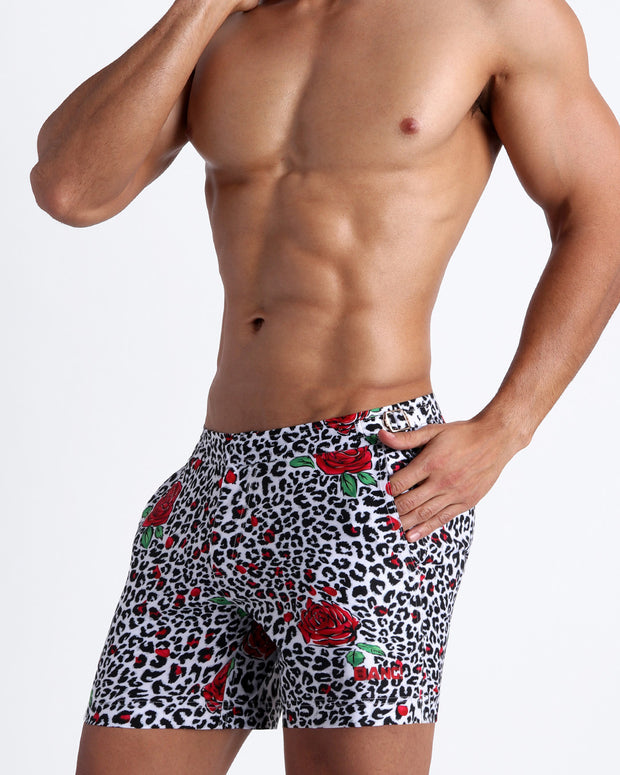 Lateral view of a man wearing the SO RED THE ROSE swim trunks by Bang! Clothes black & white leopard animal print with red roses.
