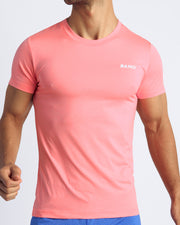 Frontal view of male model wearing the TONED CORAL in a solid light orange quick-dry workout shirt by the Bang! brand of men's beachwear from Miami.