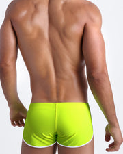 Back view of a male model wearing men’s swim shorts in neon highlighter yellow color by the Bang! Clothes brand of men's beachwear.