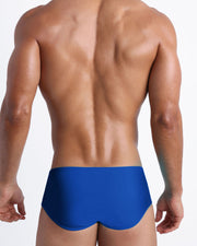 Back view of a male model wearing men’s swim sungas in cobalt color by the Bang! Clothes brand of men's beachwear.