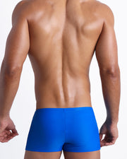Back view of a male model wearing men’s swim trunks in cobalt color by the Bang! Clothes brand of men's beachwear.