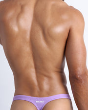Back view of a male model wearing men’s swim thongs in neon light purple color made with Italian-made Vita By Carvico Econyl Nylon by the Bang! Clothes brand of men's beachwear.