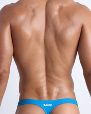 Back view of a male model wearing men’s swim thong in blue by the Bang! Clothes brand of men's beachwear from Miami.