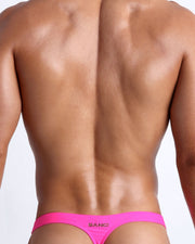 Back view of a male model wearing men’s swim thongs in bright pink color by the Bang! Clothes brand of men's beachwear.