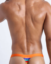 Back view of male model wearing men's beach swim bikini in vibrant orange with color stripes in yellow, bold red, aqua, and blue.