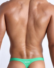 Back view of a male model wearing men’s swim thong made with Italian-made Vita By Carvico Econyl Nylon in aqua green color by the Bang! Clothes brand of men's beachwear.