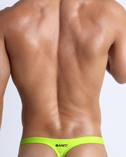 Back view of a male model wearing men’s swim thongs in neon highlighter yellow color by the Bang! Clothes brand of men's beachwear.