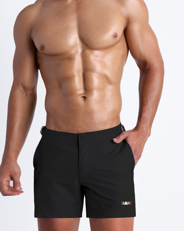 Frontal view of a sexy male model wearing a men’s beach tailored shorts in black by the Bang! Menswear brand from Miami.