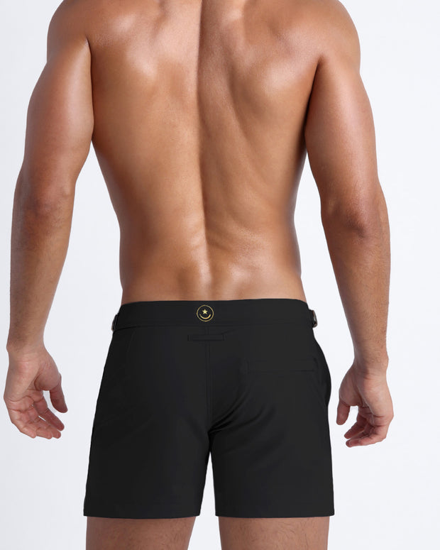 Back view of a male model wearing men’s beach shorts in black by the Bang! Clothes brand of men&