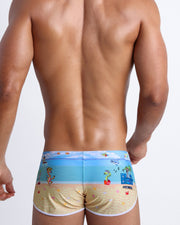 Male model's back view showing the 8-BIT WILD BEACH PARTY beach swim shorts for men with vintage  sprite graphics of  Atari video game, Nintendo, Sega, Commodore 64