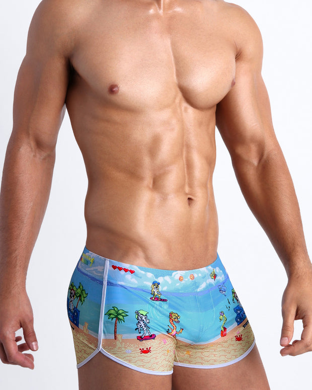 Lateral view of male model wearing the 8-BIT WILD BEACH PARTY swimming mini shorts for men, made by Bang! Miami.