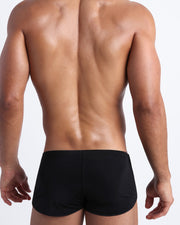 Back view of a male model wearing men’s swim mini shorts in black by the Bang! Clothes brand of men's beachwear from Miami.