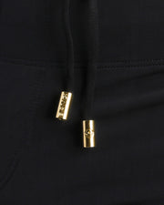 Close-up view of the DARK KNIGHT black men’s drawstring swim shorts showing black cord with custom branded golden cord ends, and matching custom eyelet trims in gold.