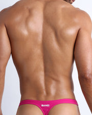 Back view of a sexy male model wearing CONFESS MAGENTA swim thong made with Italian-made Vita By Carvico Econyl Nylon from the Bang! brand of men's beachwear from Miami.