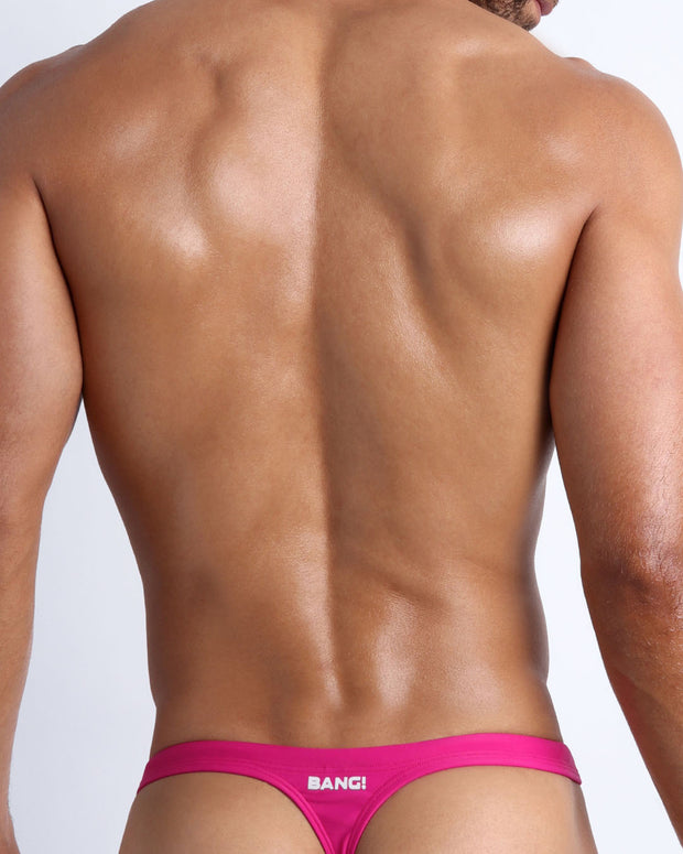 Back view of a sexy male model wearing CONFESS MAGENTA swim thong made with Italian-made Vita By Carvico Econyl Nylon from the Bang! brand of men&