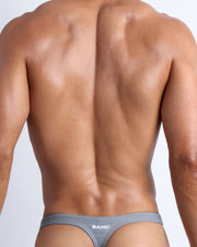 Back view of a male model wearing men’s swim thongs in stone grey color by the Bang! Clothes brand of men's beachwear.