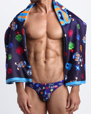 Model showing the HEY MISTER TJ (CLUB MIX) quick-dry microfiber towel with matching swim briefs for the beach with clubbing and disc-jockey details in dark colors.