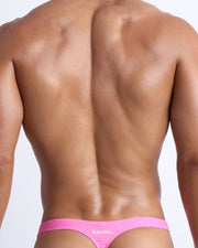Back view of a male model wearing LA BEACH EN ROSE men’s bikini swimwear in neon pink color by the Bang! Clothes brand of men's beachwear.