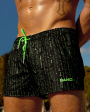 Male model at the beach wearing the MATRIX Show Shorts This swimsuit for men has multiple hidden messages within the matrix code. Official black and green matrix colors by BANG! Clothes, the official brand of men’s high-quality swimwear.