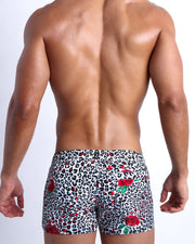 Male model's back view showing the SO RED THE ROSE swim shorts for men featuring animal print of black and white cheetah with red roses by Bang! men's swimwear.