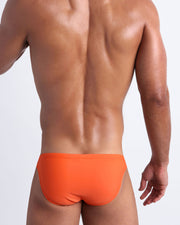 Back view of a male model wearing men’s swim mini-brief in apricot color by the Bang! Clothes brand of men's beachwear.