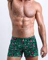 Front view of model wearing the CAMO CHAMELEON men’swim bottoms in a forest green color with white and pink camo print by the Bang! Clothes brand of men's beachwear from Miami.