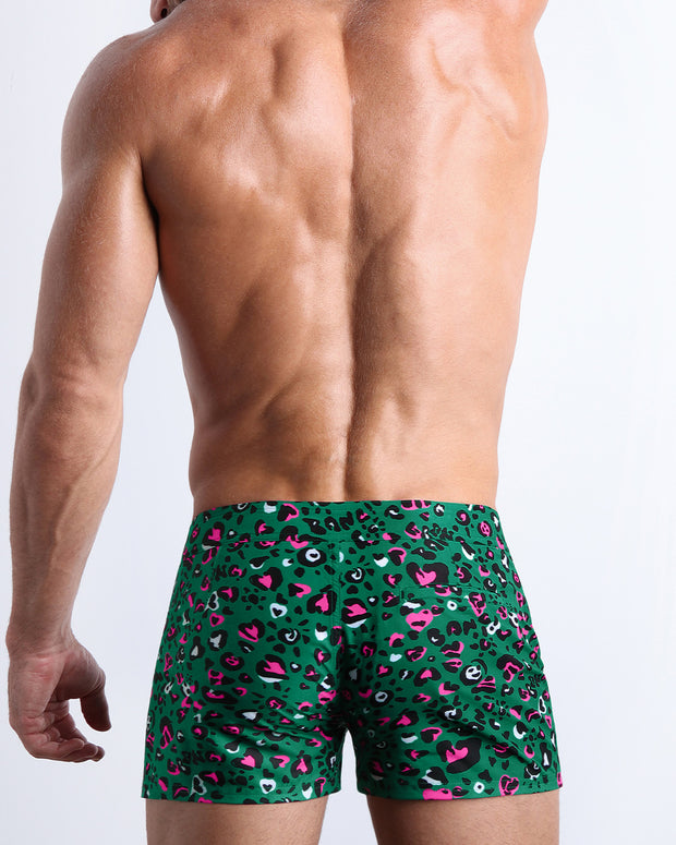 Back view of male model wearing the CAMO CHAMELEON beach shorts for men by BANG! Miami featuring in teal with pink and black animal print.