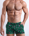 Front view of model wearing the CAMO CHAMELEON men’s beach shorts in a forest green color with white and pink camo print by the Bang! Clothes brand of men's beachwear from Miami.