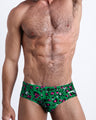 Front view of model wearing the CAMO CHAMELEON men’s bikini-style bottoms in a forest green color with white and pink camo print by the Bang! Clothes brand of men's beachwear from Miami.