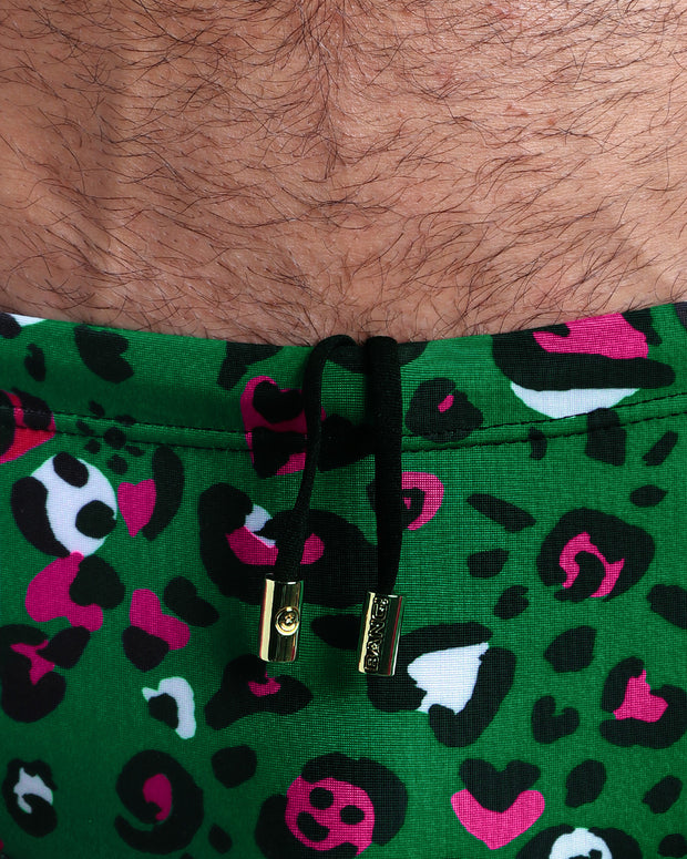 Close-up view of the CAMO CHAMELEON Swim Sunga mens swimsuit a camo green and pink color with black internal drawstring cord showing custom branded golden buttons by BANG! clothing brand.
