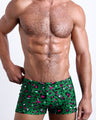 Frontal view of a sexy male model wearing men's swimsuit with mini pockets in CAMO CHAMELEON in a forest green color with white and pink camo print designed by the Bang! Menswear brand from Miami.